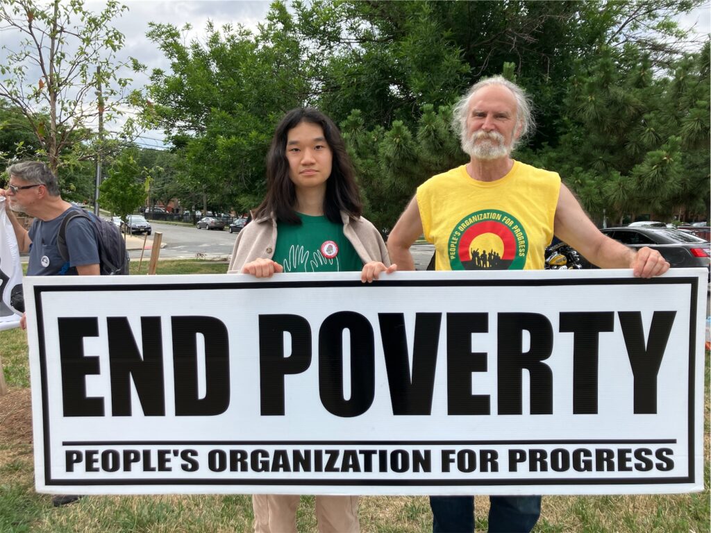Two activists hold a sign reading END POVERTY; People’s Organization from Progress.