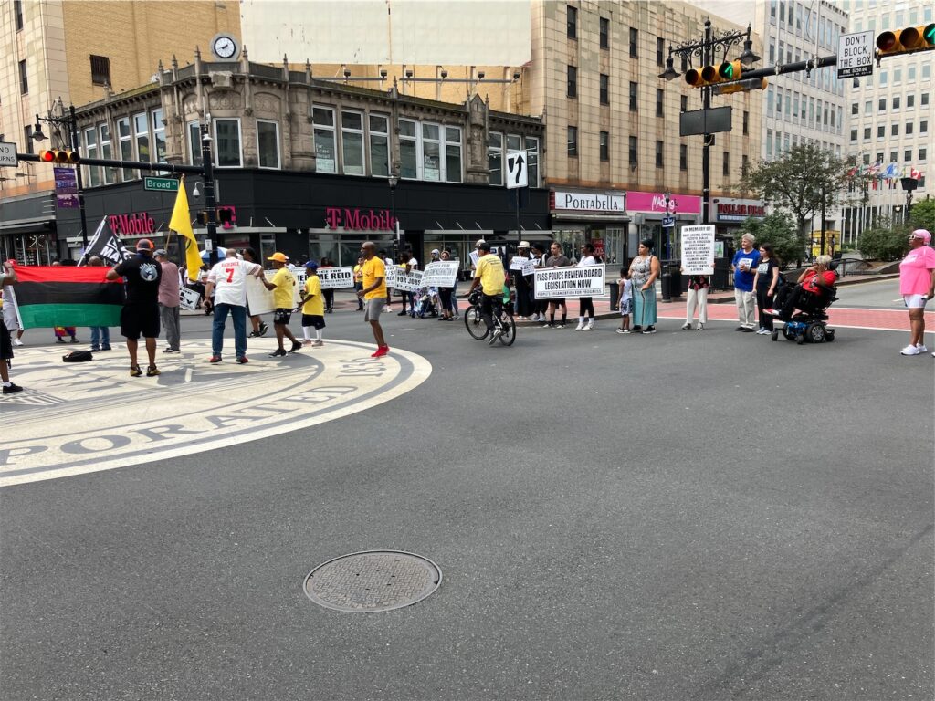 quarter of Broad and Market streets’ intersection, Newark, N.J., with PanAfrican, Black Lives Matter, and People’s Organization for Progress flags in the center, surrounded by activists, many holding POP signs with different text on each