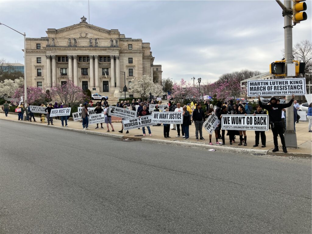Activists hold about a dozen People’s Organizaiton for Progress banners with messages honoring Dr. King and calling for justice, no more war, refusing to go back, etc.