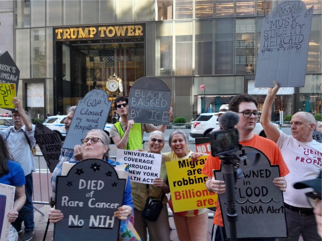 Many people holding signs in front of Trump Towner, which read “Black bagged by ICE”, “Universal Coverage through New York Health Act”, “Drowned in Flood; No NOAA Alert”, “Musk stole my Medicaid”, and more.