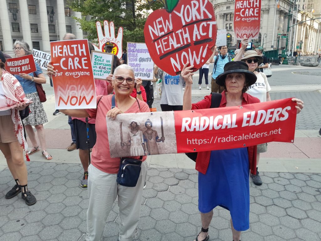 Ana and Gabriel holding Radical Elders banner and signs reading “Health Care for Everyone NOW” and “New York Health Act Now!”, in line with marchers with more signs