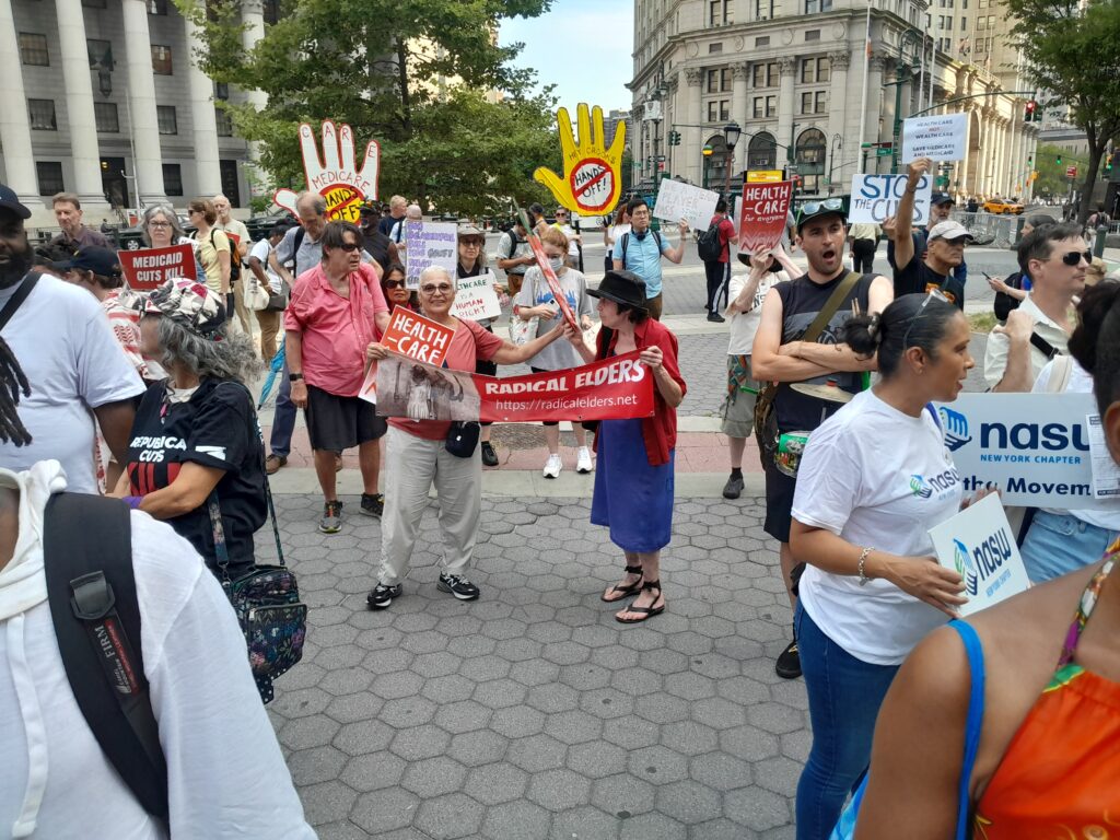 People holding signs protesting health-insurance cuts, identifying their groups, in downtown New York City