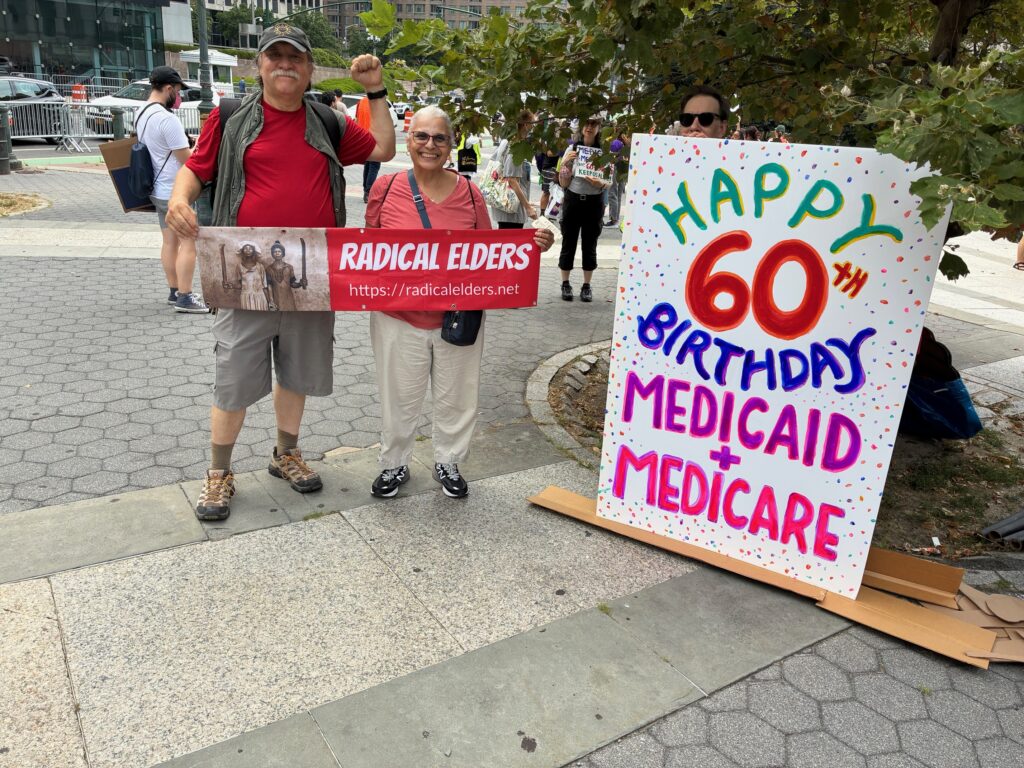 Angel and Ana holding a Radical Elders banner near someone propping up a giant sign reading Happy 60th Birthday Medicaid + Medicare
