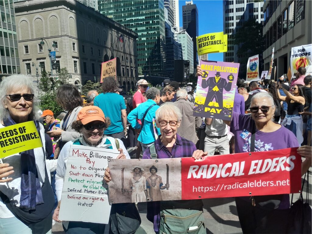 Radical Elders holding RE banner, and signs in a crowd of marchers with “Seeds of Resistance” and “Make Polluters Pay” signs