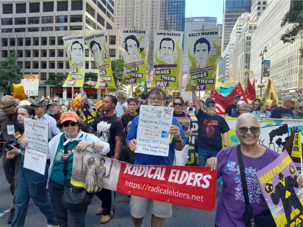 Radical Elders holding RE banner and handmade signs in front of marchers with signs saying “Make Them Pay” and cartoons of Harold Hamm, Richard Kinder, Jim Ratcliffe, Amin Nasser, and Kelcy Warren