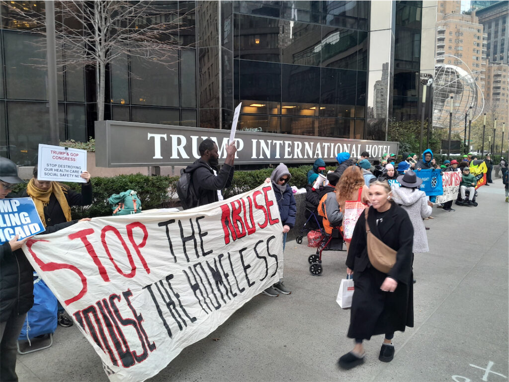ralliers outside Trump International Hotel, in foreground a banner reads “Stop the abuse. House the homeless.”