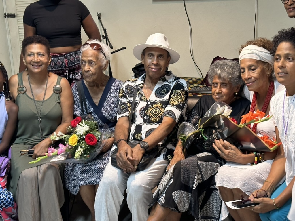 Group of 6 elders sitting together, some holding flowers.