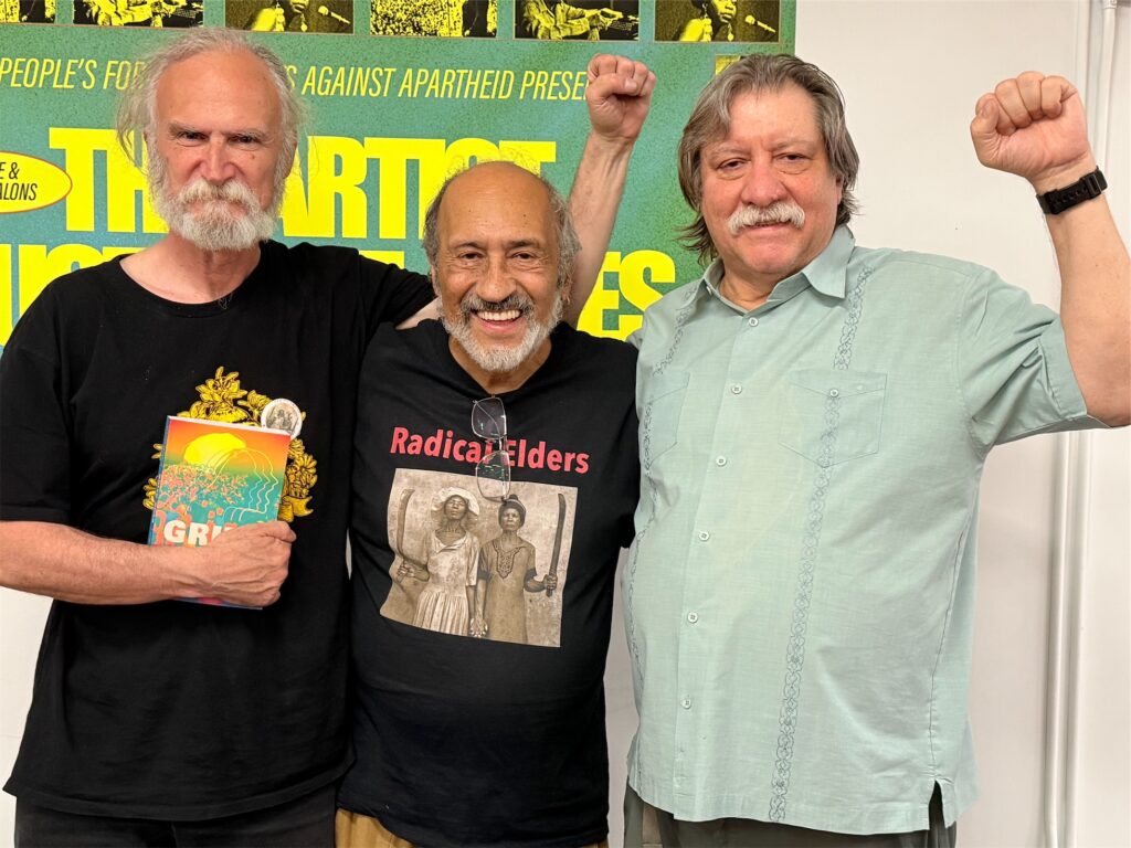 3 Radical Elders men with raised fists, holding book “Grito 2048” by RE member Maritza Arrastia