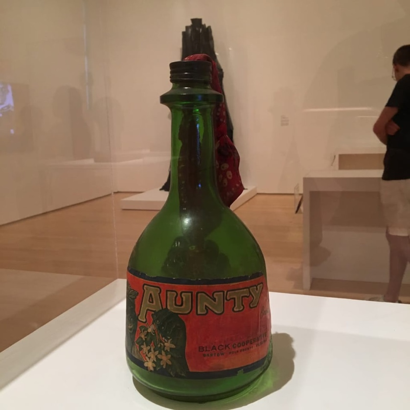 The Liberation of Aunt Jemima: Cocktail combines the iconography of the Black Power Movement, political violence, and aspirational middle-class American culture. It uses them to critique the racist stereotypes of black femininity and speak to the revolutionary aims of Black Liberation movements. Featuring a handmade label with a “mammy” figure on the front and a Black Power fist on the back, the ubiquitous California wine jug turned Molotov cocktail wryly comments on the potential and promise of armed resistance to oppression.
(description from Brooklyn Museum)